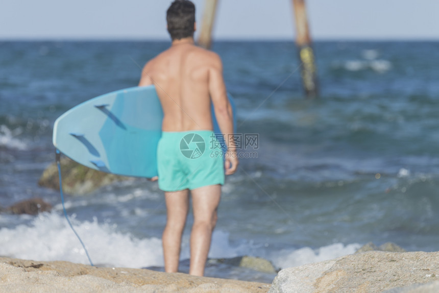 年轻冲浪者拿着蓝色冲浪板背影图片