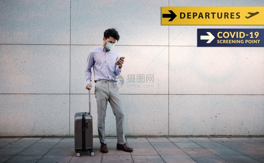 常设Corona状况概念年轻乘客商人在机场出境标志和Covid19检查站时用手持智能话和行李驾驶器的外表面具戴科作为背景生病的疾图片