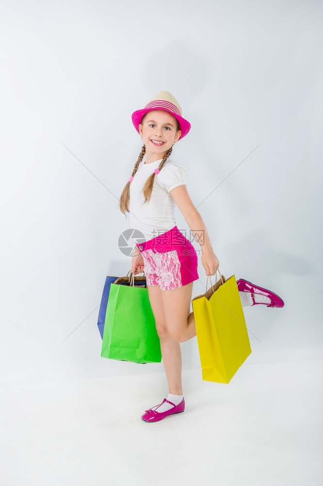 卖出可爱的姑娘在白色背景上着很多袋子画上一个孩在购物上的肖像卖出可爱的女孩和许多袋在白色背景上消费者礼物买方图片