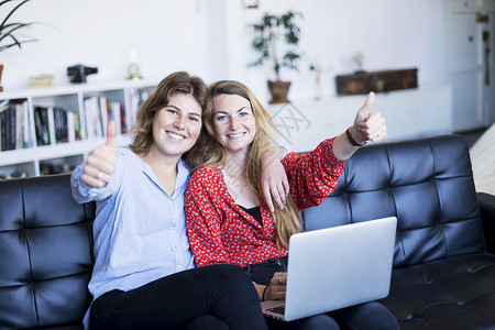 数字的对话象征带着笔记本电脑坐在沙发上做胜利标志的少女们图片