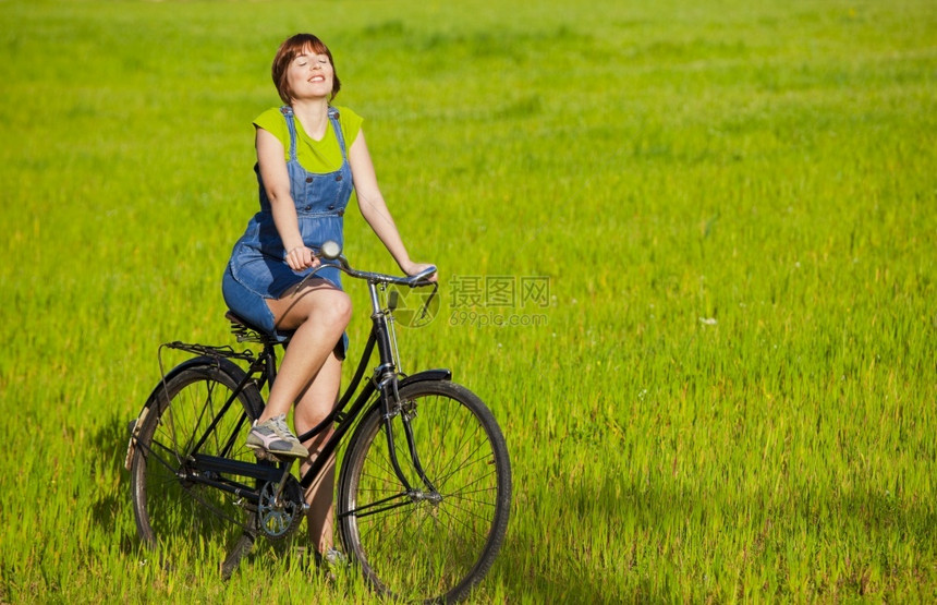 年轻女人骑着老旧自行车在绿色草地上放松成人场自然图片