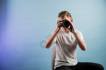 服用英俊的年轻摄影师在蓝色背景上使用相机影楼拍照图片