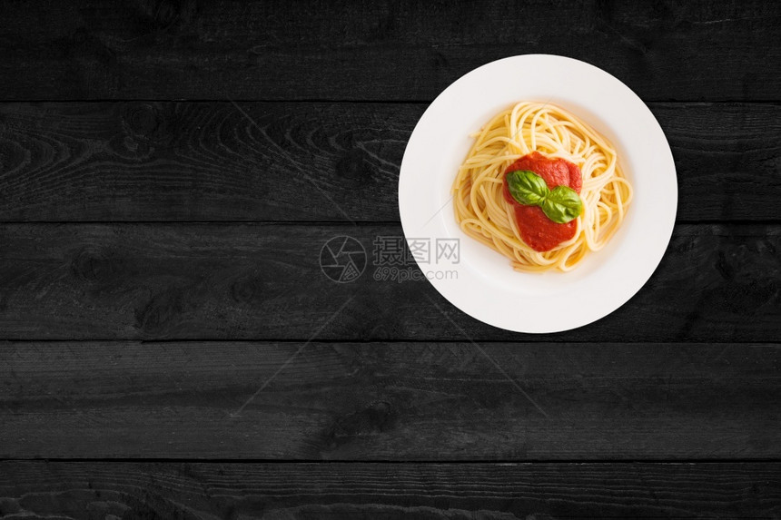 黑木桌上隔着番茄酱的意大利面贴近视线生煮熟的盘子图片
