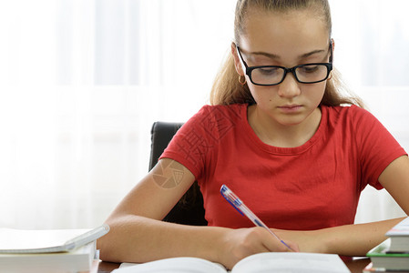 女学生桌子美丽的女孩正在写家庭作业或者在书桌上的笔记本里做时髦的图片