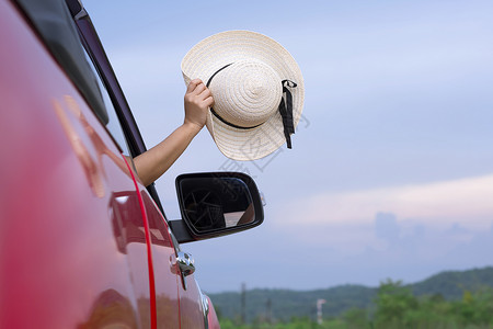 出去粘着女士亚洲手伸出红色车窗外挥舞着她宽阔的帽子山上模糊天空蓝图片