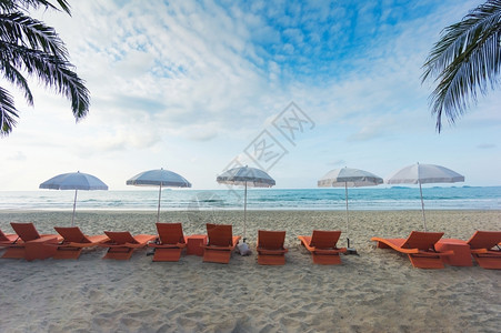 沙滩上的橙色海椅和阳伞天空海面多云的蓝色天和大海滨泡沫热带图片