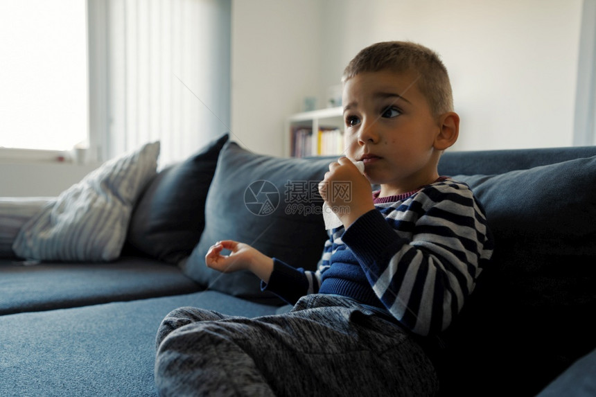 湿的坐在家沙发床上手拿着湿擦纸巾在吃边视后洗嘴和消毒脸朝清洁和消毒的一对三岁幼小Caucasian男孩的肖像预防天图片