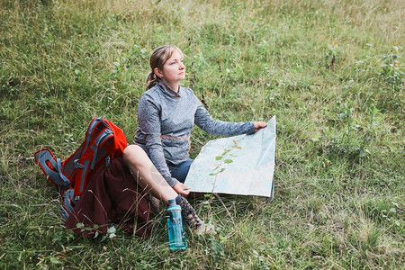 漫步徒旅行坐着在山上时背包有间休息的妇女在暑假日看着坐草地上的图图片