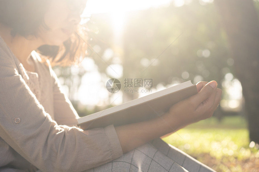 身戴眼镜的亚裔妇女坐在公园太阳落下时正在草地上阅读一本书吸引人的夏天图片