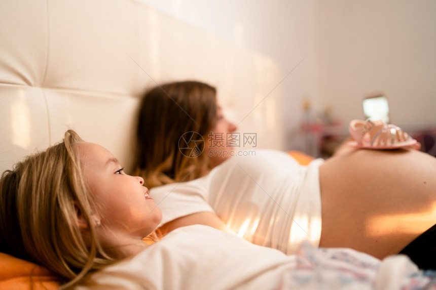 爱家庭怀孕的妇和年幼女儿在床上睡觉玩得开心用智能手机拍自照片电话图片