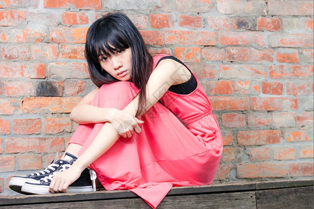 伤心坐在红砖墙边的年轻亚洲妇女感到沮丧和悲伤脸强调图片