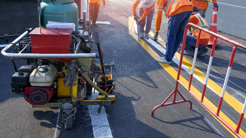 建造配有热塑料喷雾路标识机器的道工人小组正在努力沥青公路上油漆交通线在街道表面铺设铁轨跨越的沥青公路铁屏障图片