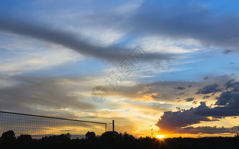 夏季日落天空中闪烁的云层横扫树木和海滩排球网的光影气候如画丰富多彩的图片