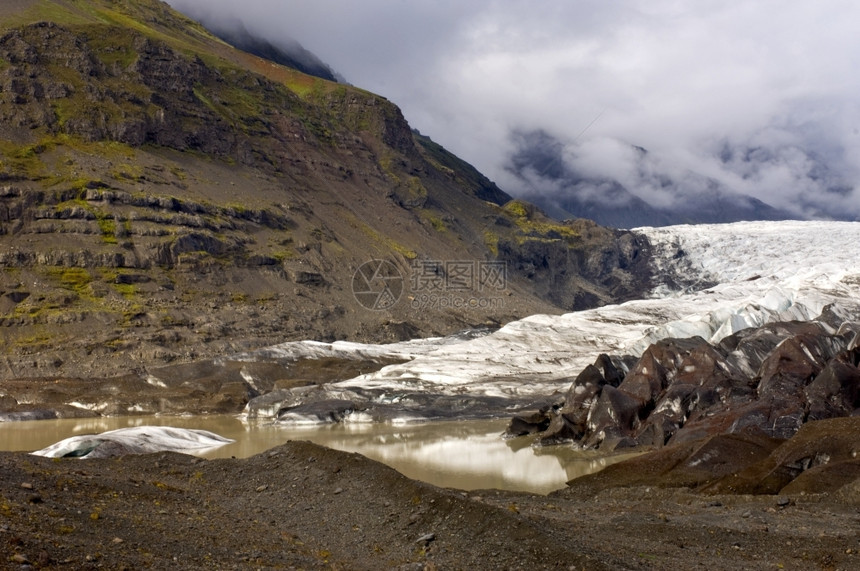 嘴苔原冰岛Svinafellsjokul的尽头有一个泥水池冰山和Moraines冰山和Moraines在一个铺天盖地的被束阳光照图片