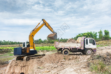 工作桶黄色挖掘机将土壤装入建筑工地的倾卸卡车中活动高清图片