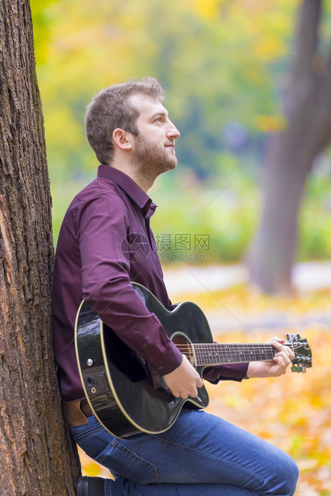 绿色年轻人坐在城市公园里弹声吉他专注的眼睛玩浪漫图片