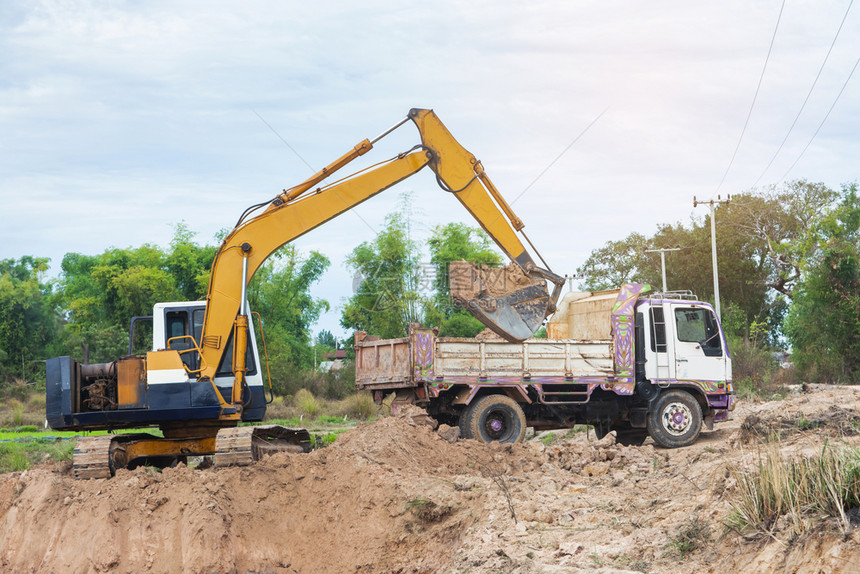 一种追踪力量黄色挖掘机将土壤装入建筑工地的倾卸卡车中图片