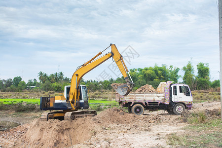 黄色挖掘机将土壤装入建筑工地的倾卸卡车中装载机项目路图片