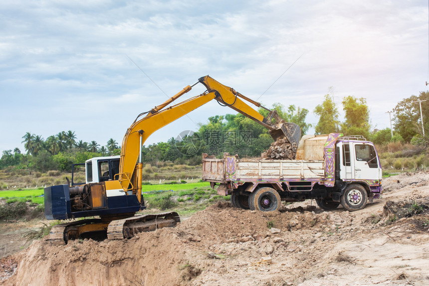 运输黄色挖掘机将土壤装入建筑工地的倾卸卡车中球建造图片