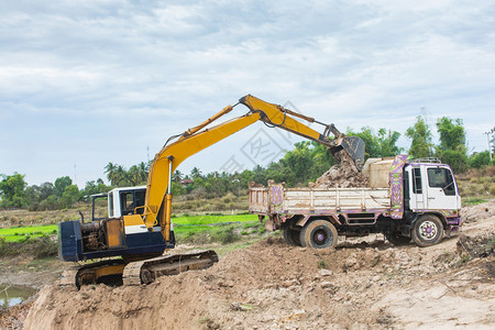 自然地球黄色挖掘机将土壤装入建筑工地的倾卸卡车中辆图片