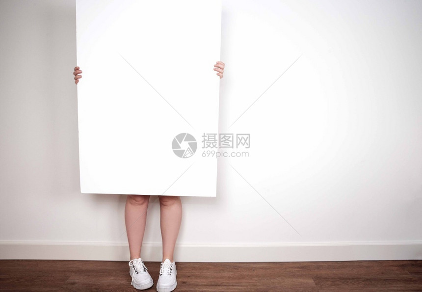 现代的床单在房间内部空中年轻女手持空白海报板或文本框靠在白墙上用于文本品牌推广图片
