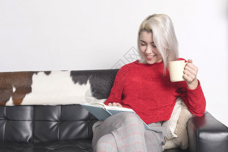 金发女人在皮革沙上读书金女郎自在室内的图片