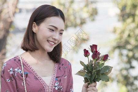 正畸微笑的亚洲女在公园看到红玫瑰成人绿色图片