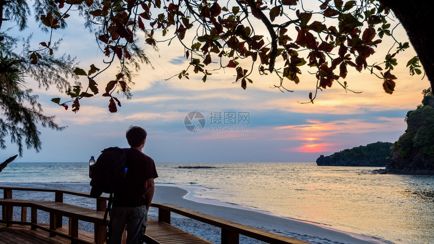 红色的一名带背包男子旅行者正站在泰国佐顿KohTarutoo岛天上的太阳看着泰国Tarutao岛日落的169个宽屏幕旅行者看着T图片