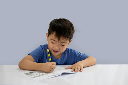 亚洲男孩正在写一些关于蓝背景孤立的书但中写着笔勤奋美丽的图片