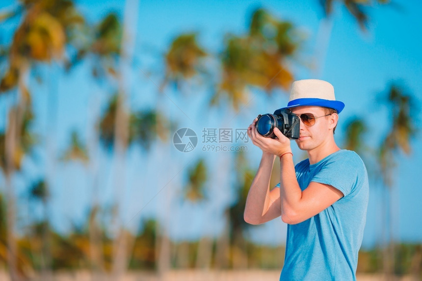 年轻男子在热带海滩拍摄照片年轻男子在热带海滩拍摄影机的照片椰子休息喜悦图片