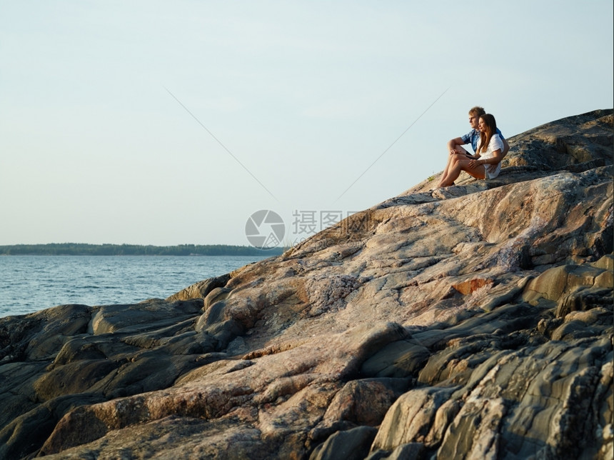 年轻夫妇坐在悬崖上群岛的岩石岸边户外天空美丽的图片