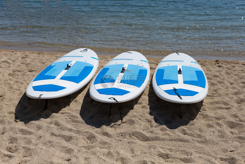 三块白色冲浪板搁在海滩上图片