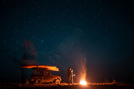 欢乐的情侣女站在星空前燃起的营火中享受着宁静的夜晚背景