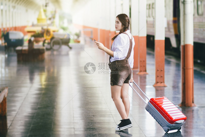 移动的细胞女在火车站旅行中亚洲孕妇旅行时持有带红色手提箱的智能机图片