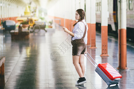 移动的细胞女在火车站旅行中亚洲孕妇旅行时持有带红色手提箱的智能机图片