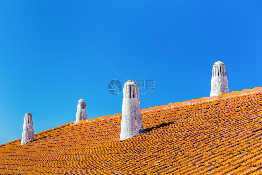 四根白色烟囱和蓝天空的橙色屋顶砖外部面覆盖图片