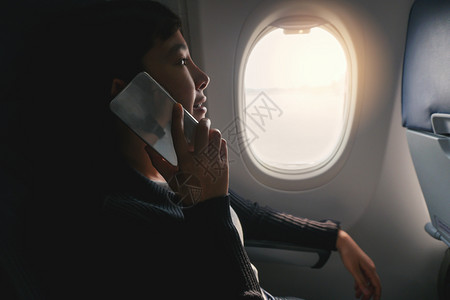 坐在飞机窗口附近行时使用智能电话的亚洲女旅游客班级乘航空公司图片