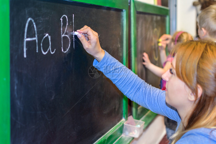 学习男生老师教孩子们在学校的黑板上写字母给学生们讲书写字母课堂图片
