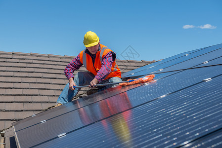 安全屋安全在屋顶上打扫太阳能电池板的青年工人关注面板橙背景