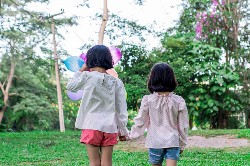 夏天闲暇可爱的两名女孩在公园户外的内持有多彩玩具气球图片