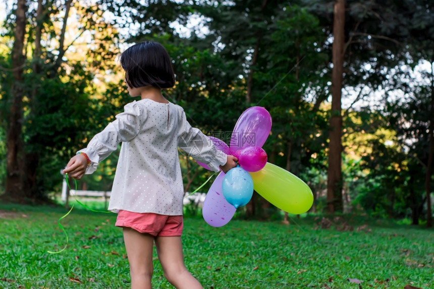 俏皮积极的女孩在公园户外露天拿着多彩的玩具气球抓住图片