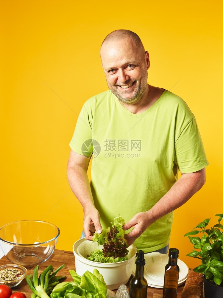 烘干机男人成餐桌上新鲜沙拉成分中年人烹煮沙拉和用旋转干燥机复制空间和黄色背景图片