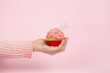 女手上的美味纸杯蛋糕在浅粉红背景上单色节食概念与纸杯蛋糕和粉霜复制空间一色快乐概念以及纸杯蛋糕和粉霜空间派对工作室待背景