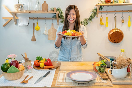 亚洲年青做饭在现代厨房食品和健康概念中展示沙拉并介绍年轻的蔬菜女孩图片