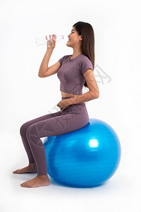 坐在瑜伽球上喝水的年轻女子图片