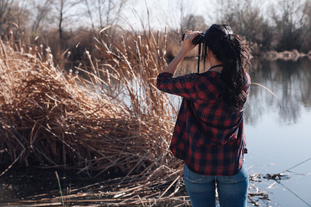 穿着双目望远镜和格子衬衣的湖角码头上黑发年轻女人快乐的搜索衬衫图片