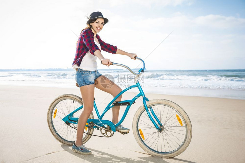 潮人一个有魅力的年轻女子在海滩上骑着自行车漂亮的海洋图片