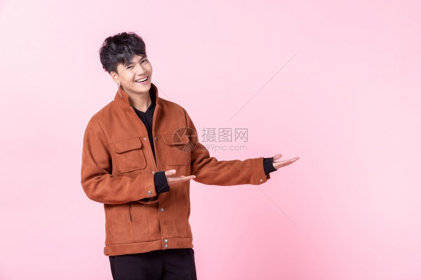 成人一个英俊的亚洲男子英俊的年轻男子用两手和指对着侧眼看在爱中孤立的相机在粉红色空白复制间室背景快乐的愉图片
