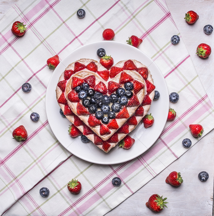 新鲜的以蓝莓和草心脏形式白板上的盘子粉红餐巾纸上带条纹的彩色面巾纸背景馅饼粉色的图片