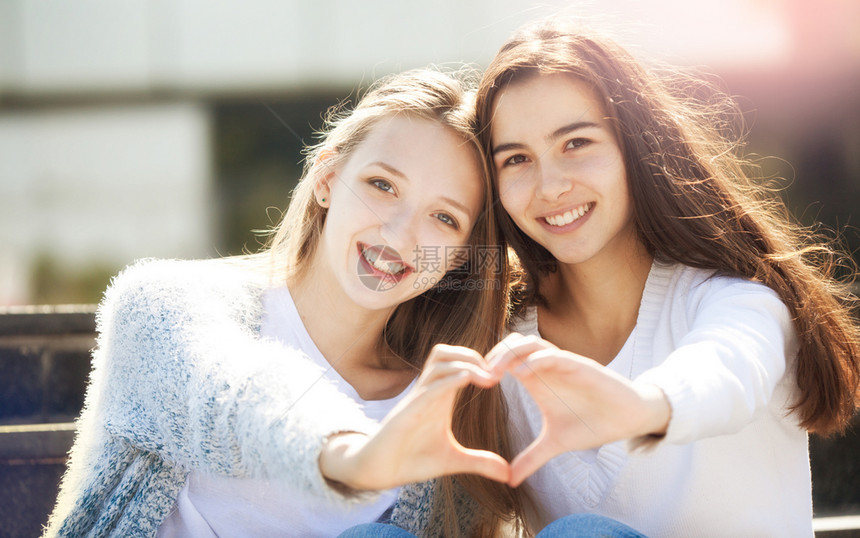 两个年轻女握手在心脏和微笑的形状中看着镜头笑声女孩友谊青少年图片